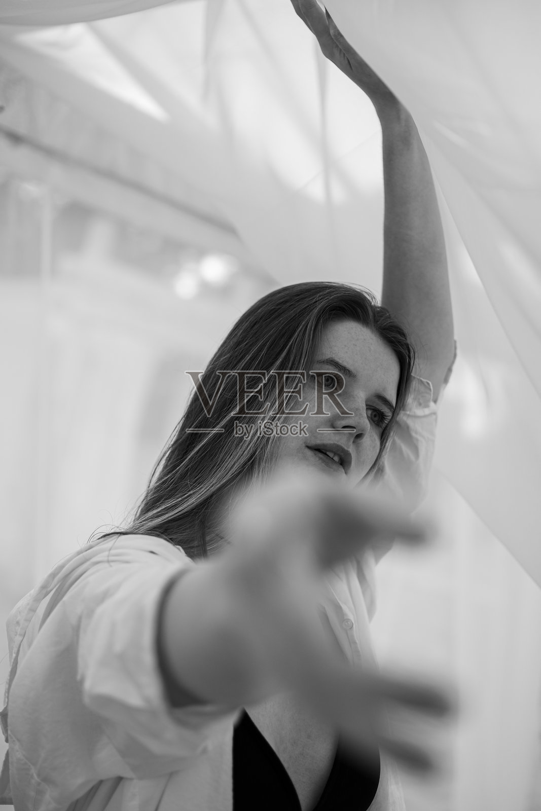 一位迷人的长发女孩在水边的海滩上漫步的肖像。穿着泳衣和衬衫的年轻女性在河边迎接夏日的黎明。黑白照片。照片摄影图片