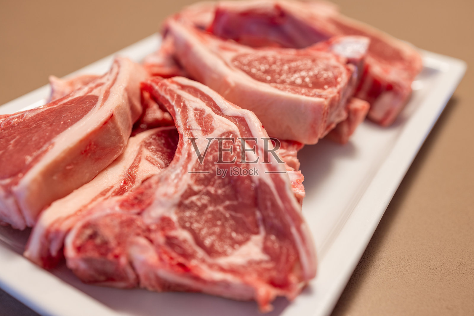 几块生羊排放在白色盘子上，肉质呈现大理石纹的粉色，脂肪清晰可见，准备烹饪。照片摄影图片