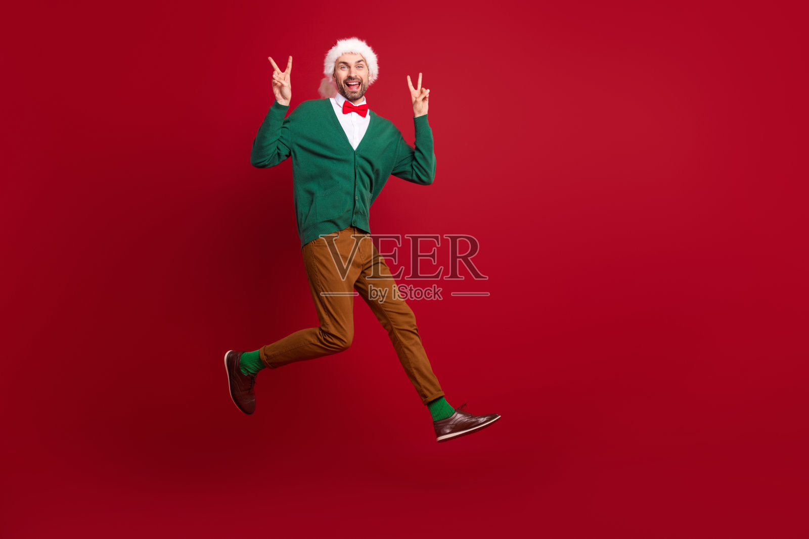 全身照，轻松兴奋的男孩在红色背景上跳跃，双手比出V字手势。照片摄影图片