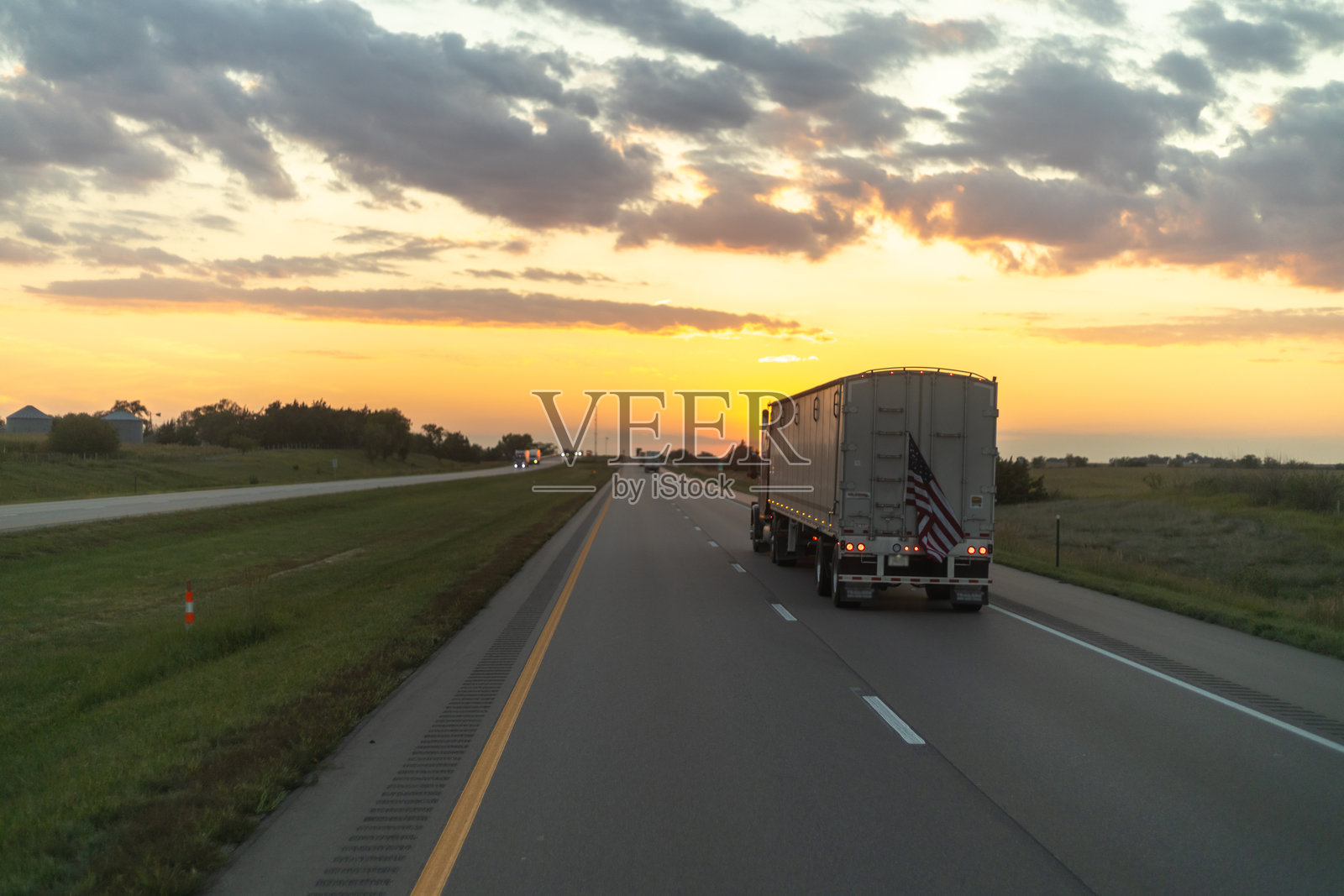 一辆半挂卡车在高速公路上行驶，背景是壮丽的日落天空，展现了长途运输的美丽。照片摄影图片