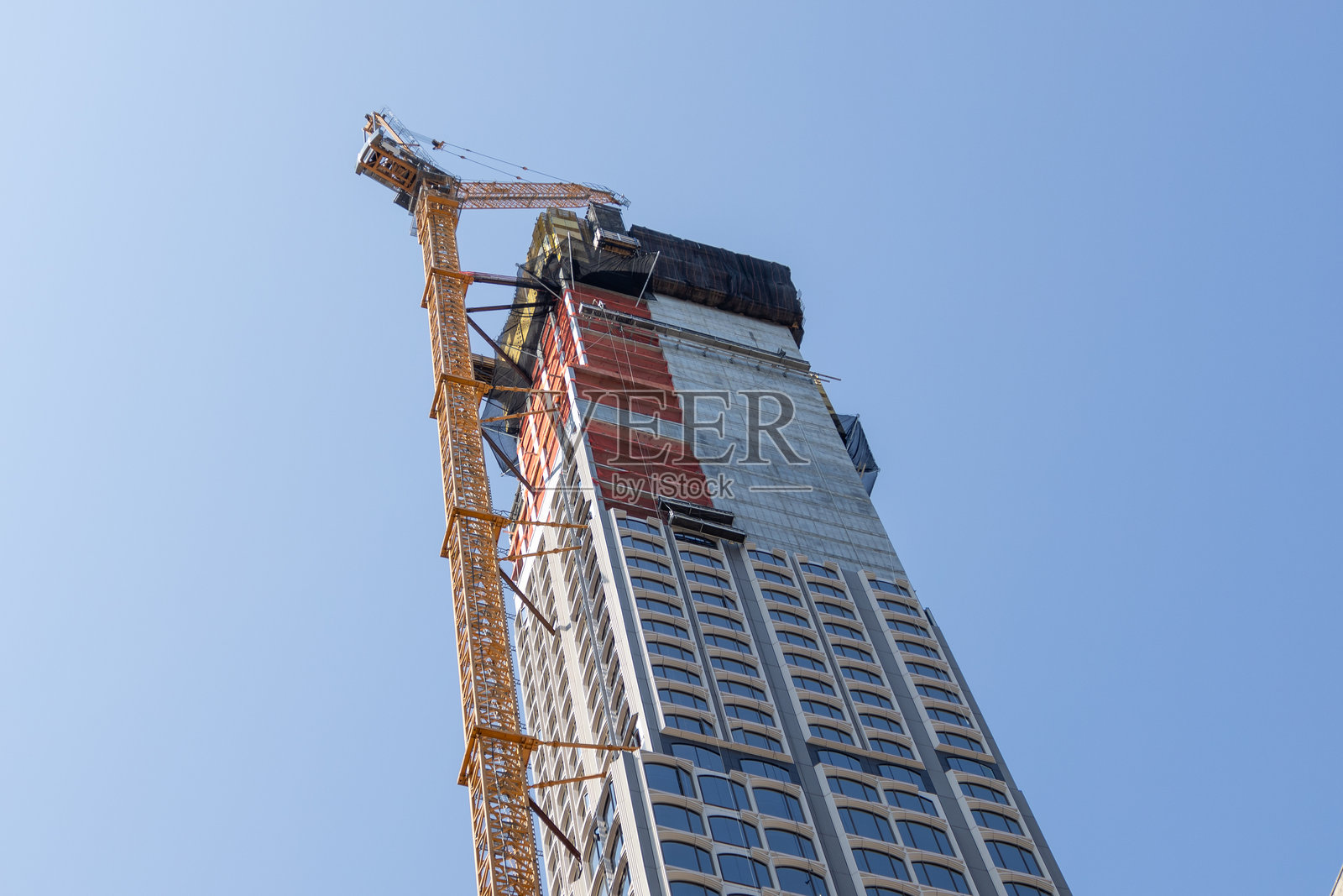 繁忙城市环境中，高楼大厦建设场景，起重机在晴朗的天空下作业。照片摄影图片