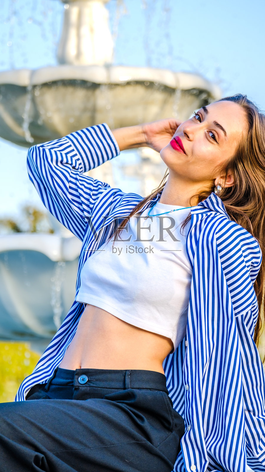 一位美丽的年轻女性在阳光明媚的树木繁茂的公园里为镜头摆姿势照片摄影图片