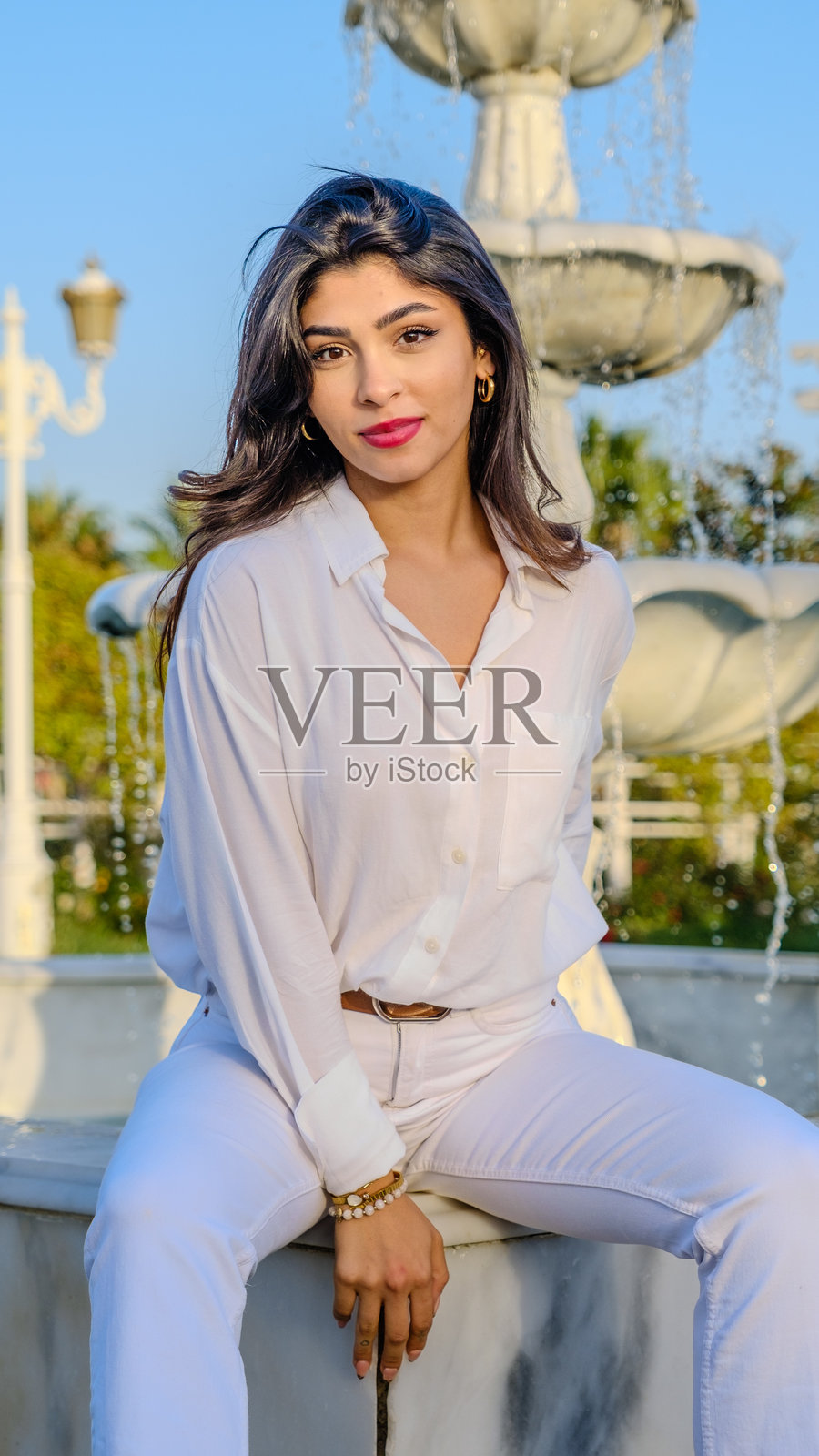 一位美丽的年轻棕发女性在阳光明媚的树木繁茂的公园里为镜头摆姿势照片摄影图片