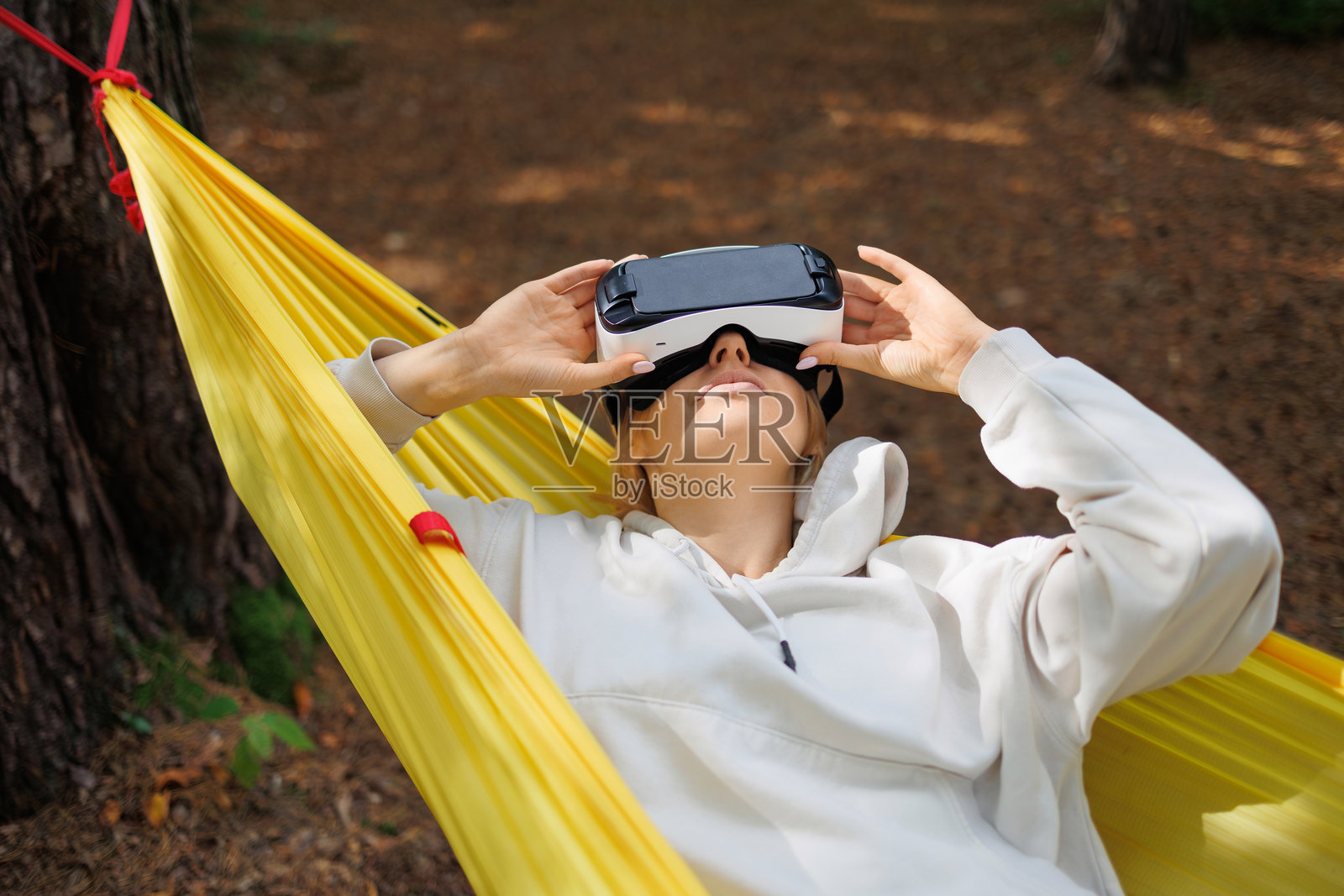 一位年轻女性戴着虚拟现实眼镜，躺在森林中的吊床上。照片摄影图片
