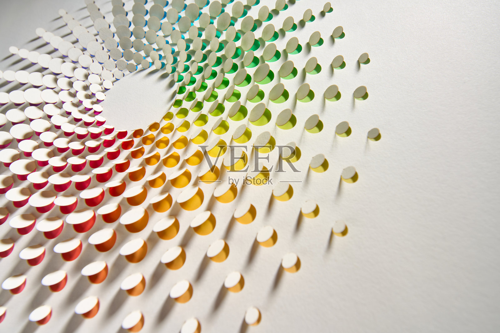 圆形纸艺作品，色彩斑斓的彩虹渐变圆点在白色背景上投射出复杂的阴影。照片摄影图片