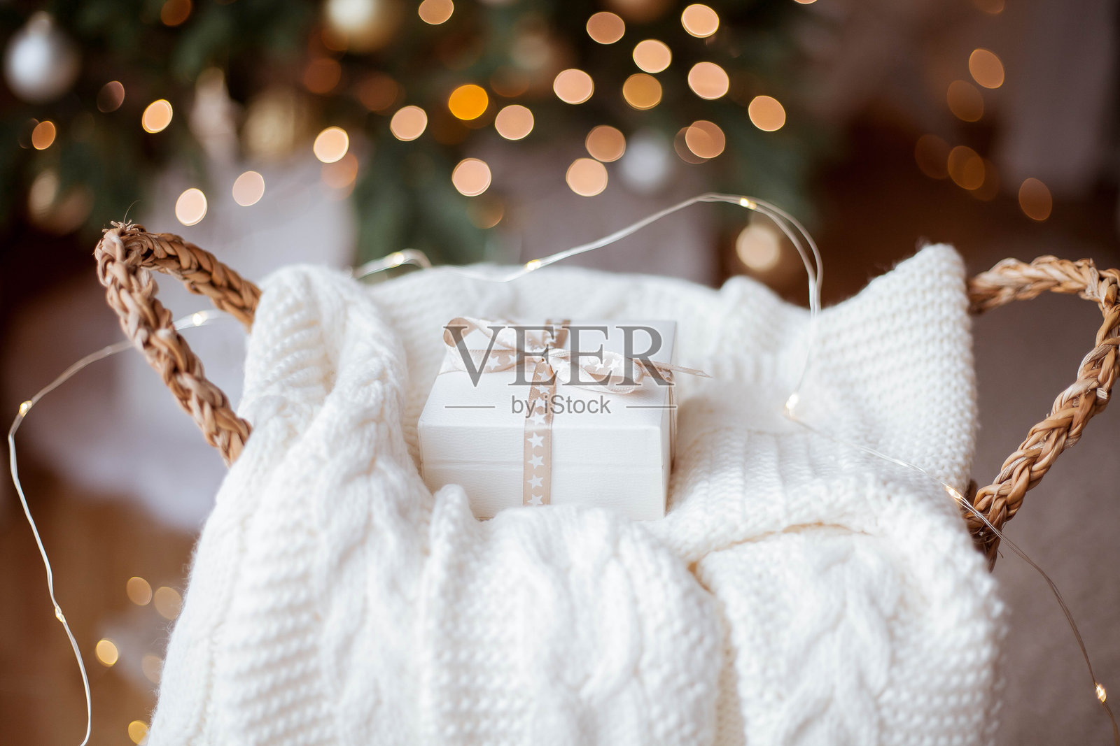 圣诞节温馨家居装饰。灯光，圣诞树。冬季假期。带丝带的小白礼盒，针织毛衣，藤编篮子。照片摄影图片