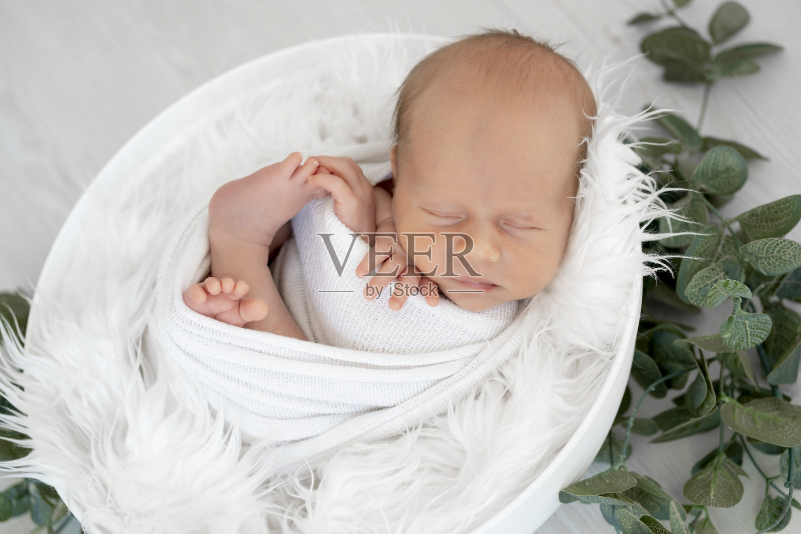 一个新生儿躺在床上的尿布里，背景为白色孤立，留有文字空间，一个小男婴正在甜美地睡觉。照片摄影图片