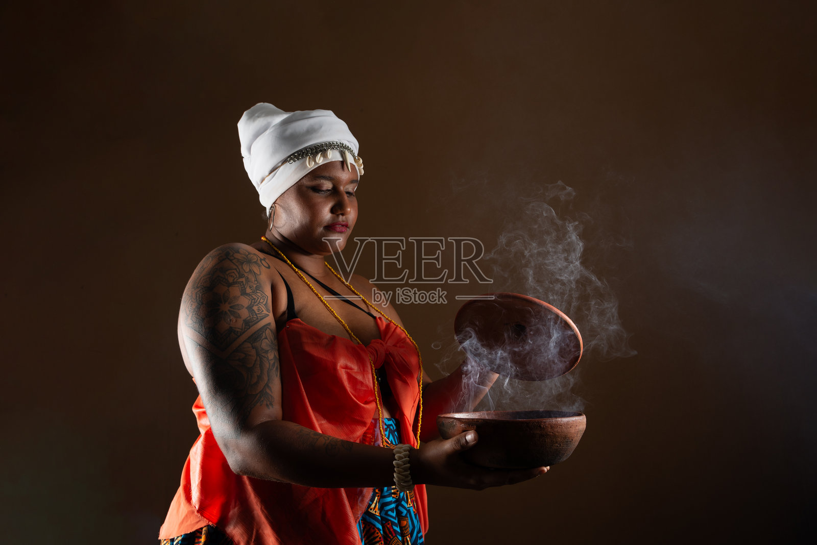 身穿传统坎东布雷服饰的美丽女性，正在打开一个冒烟的陶罐。照片摄影图片