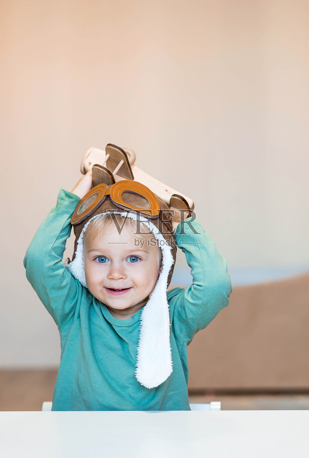 一个两岁的小男孩戴着飞行员帽，正在玩一个木制飞机和一个物流积木。儿童木制玩具有助于儿童发展。照片摄影图片