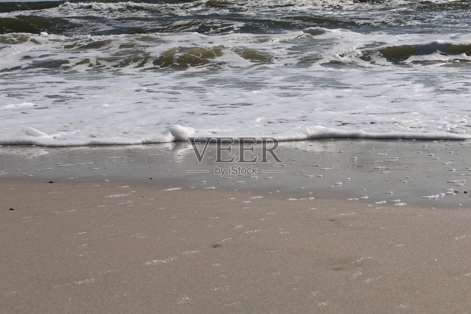 温柔的海浪拍打着光滑的沙滩，蓝天清澈如洗照片摄影图片