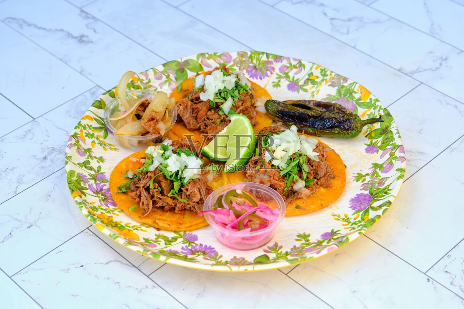 美味的墨西哥牛肉塔可，配有墨西哥胡椒、香菜和新鲜青柠，盛放在圆形花卉盘上照片摄影图片