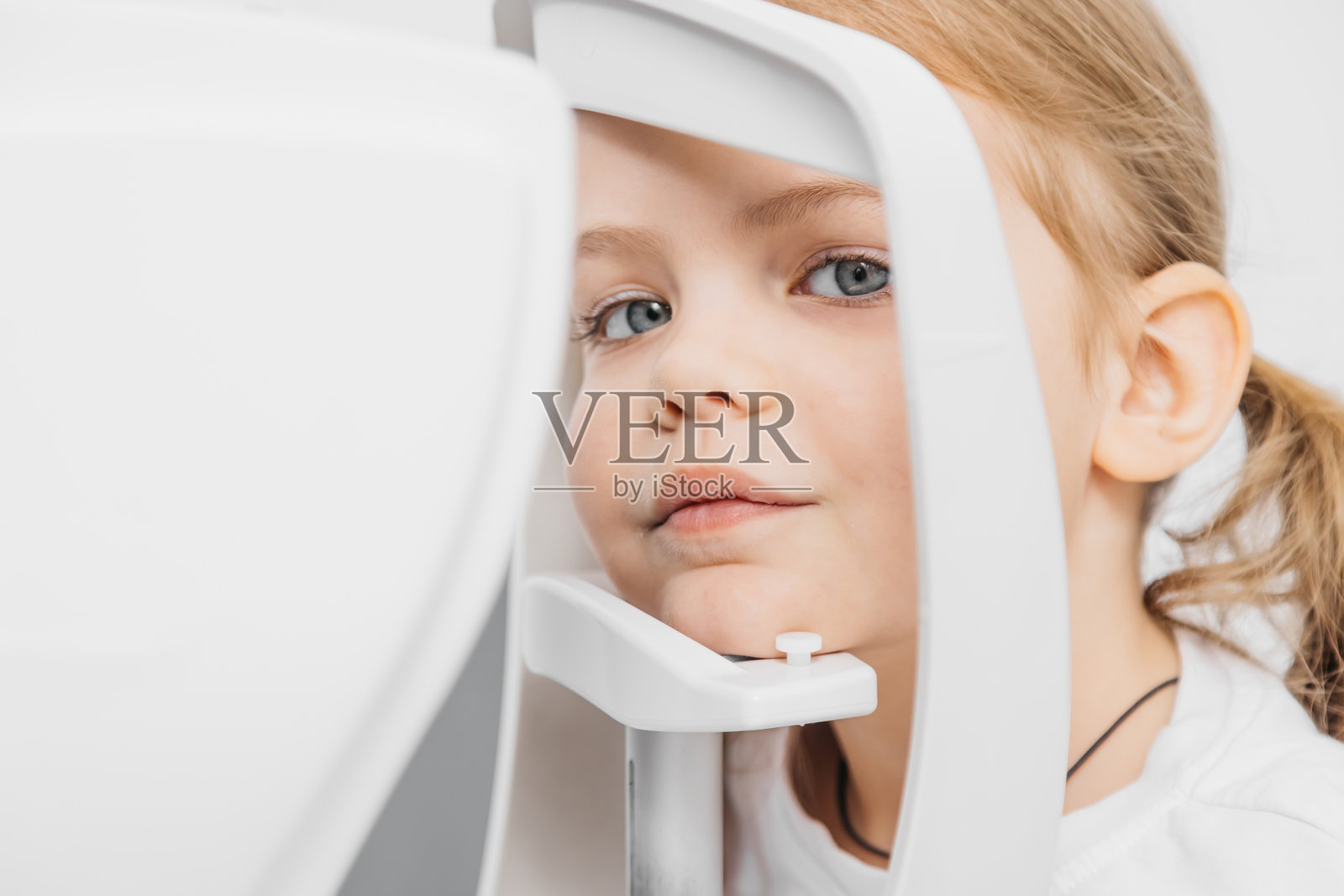 一位儿科验光师使用现代设备为小女孩检查眼睛。快乐的小女孩看起来很舒适，强调了在儿科眼科检查中的安全感和自信心。照片摄影图片