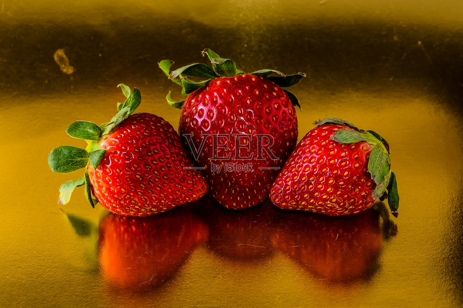 三颗红草莓在金色背景上照片摄影图片