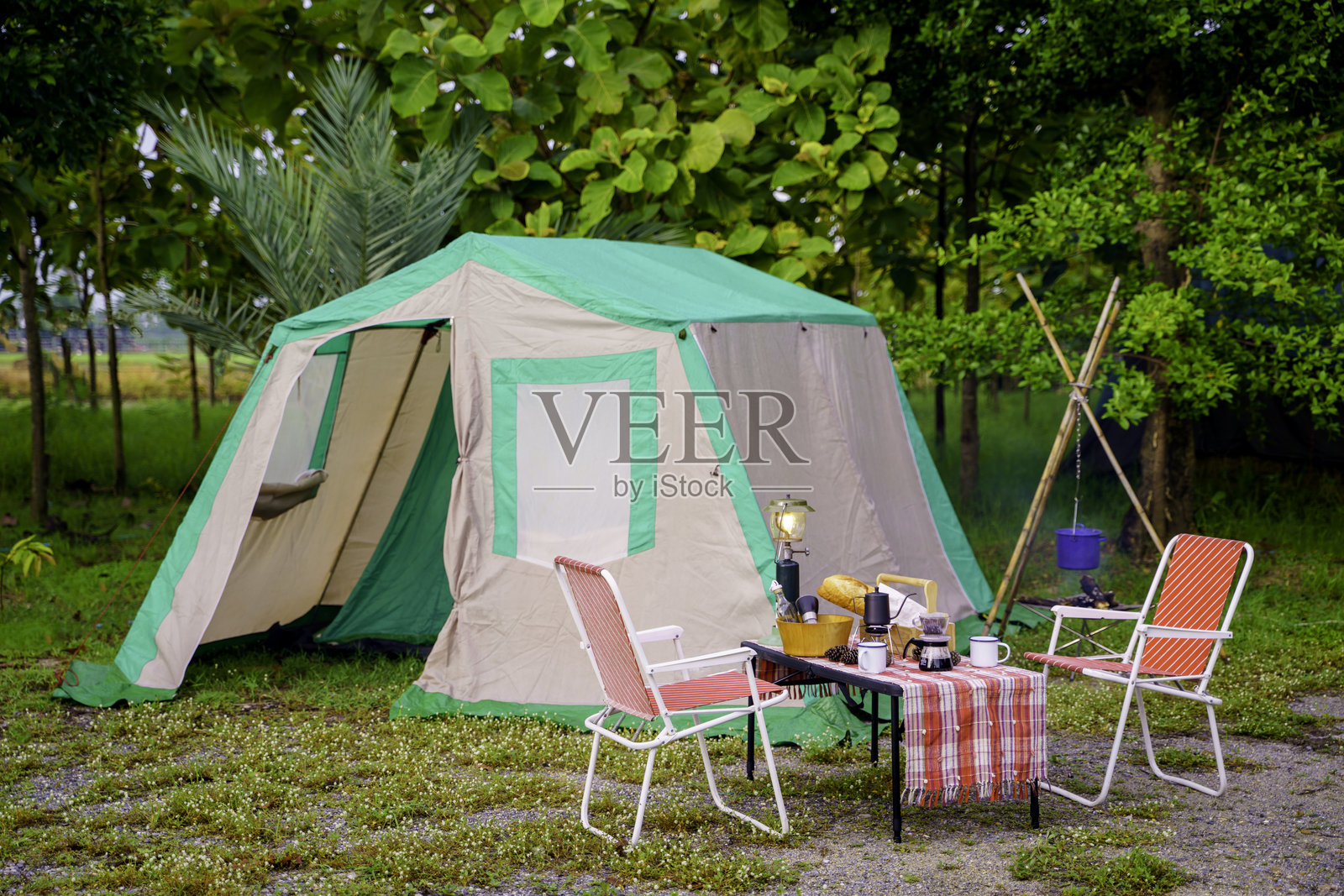 夜晚的露营帐篷、老式小屋帐篷、古董灯笼、复古椅子和森林中木桌上的户外咖啡设施照片摄影图片