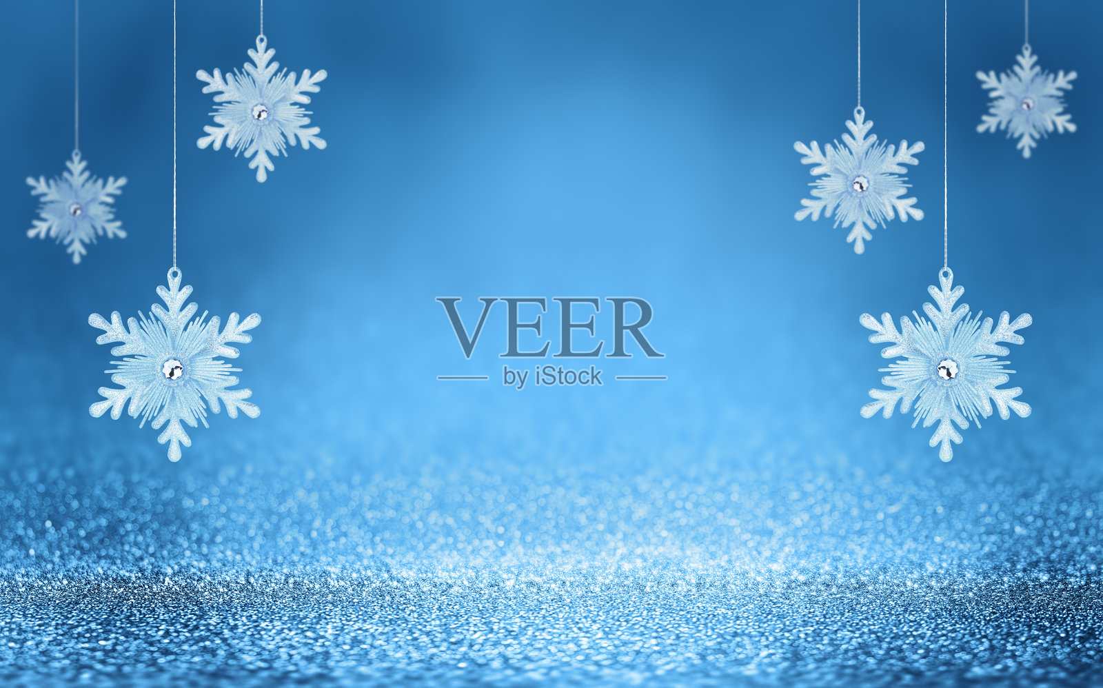 悬挂在闪亮蓝色背景上的圣诞雪花，伴有散景灯光。节日冬季假日装饰和饰品。照片摄影图片