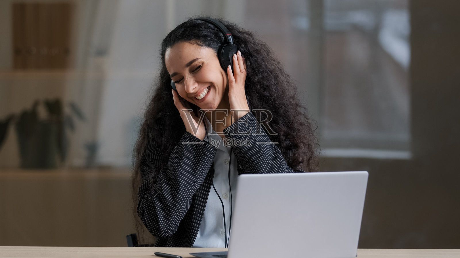 快乐的年轻阿拉伯女性自由职业者，戴着耳机，听着大声音乐，自由地在办公室唱歌，轻松的手部动作，浪费时间，享受工作间隙的概念。照片摄影图片