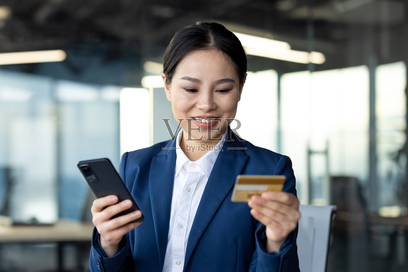 亚洲女商人在办公室环境中使用智能手机和信用卡，强调在线银行业务和专业商业，展现自信和现代金融科技。照片摄影图片