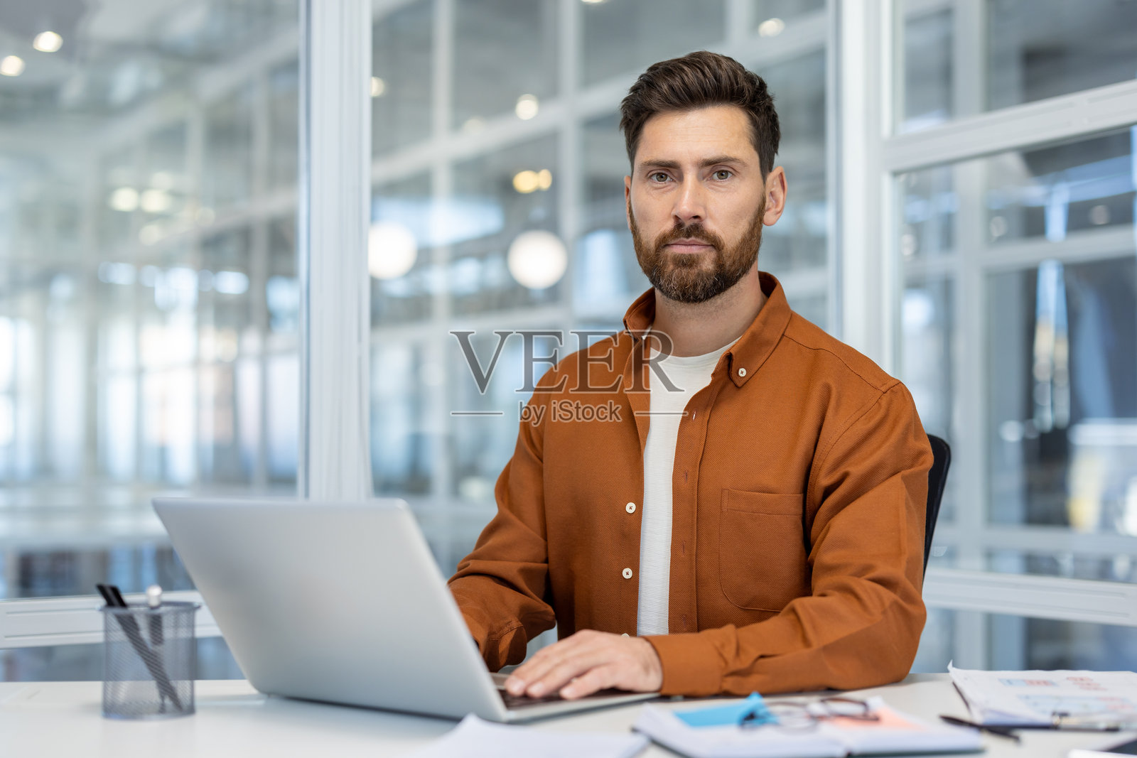 年轻商人在现代办公室里穿着休闲衬衫，专注地使用笔记本电脑工作照片摄影图片