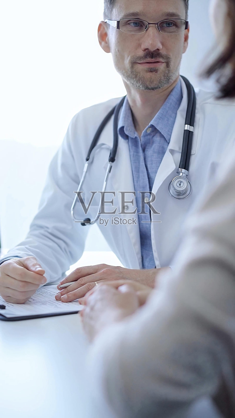 医生与患者。医生穿着白色的医用外套，里面是蓝色衬衫，在诊所咨询时用手势表达。医学概念照片摄影图片
