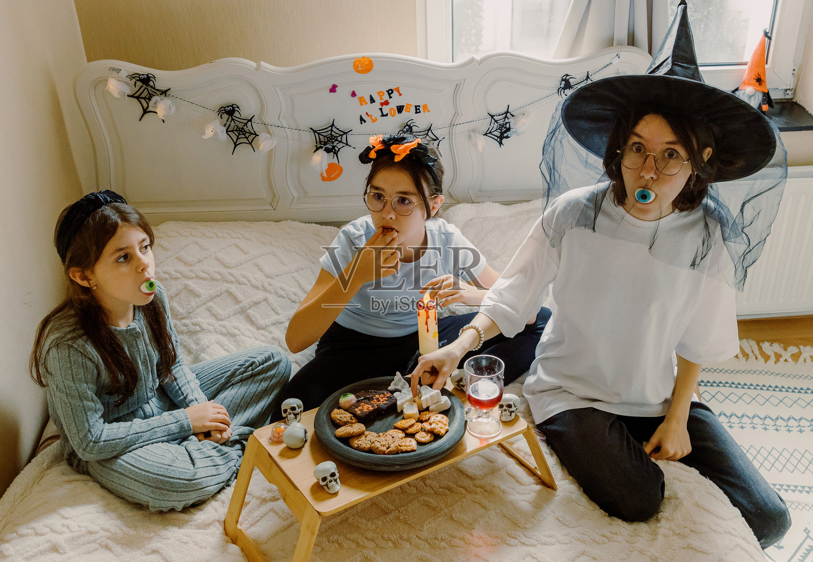 三个女孩坐在床上吃万圣节早餐零食。照片摄影图片