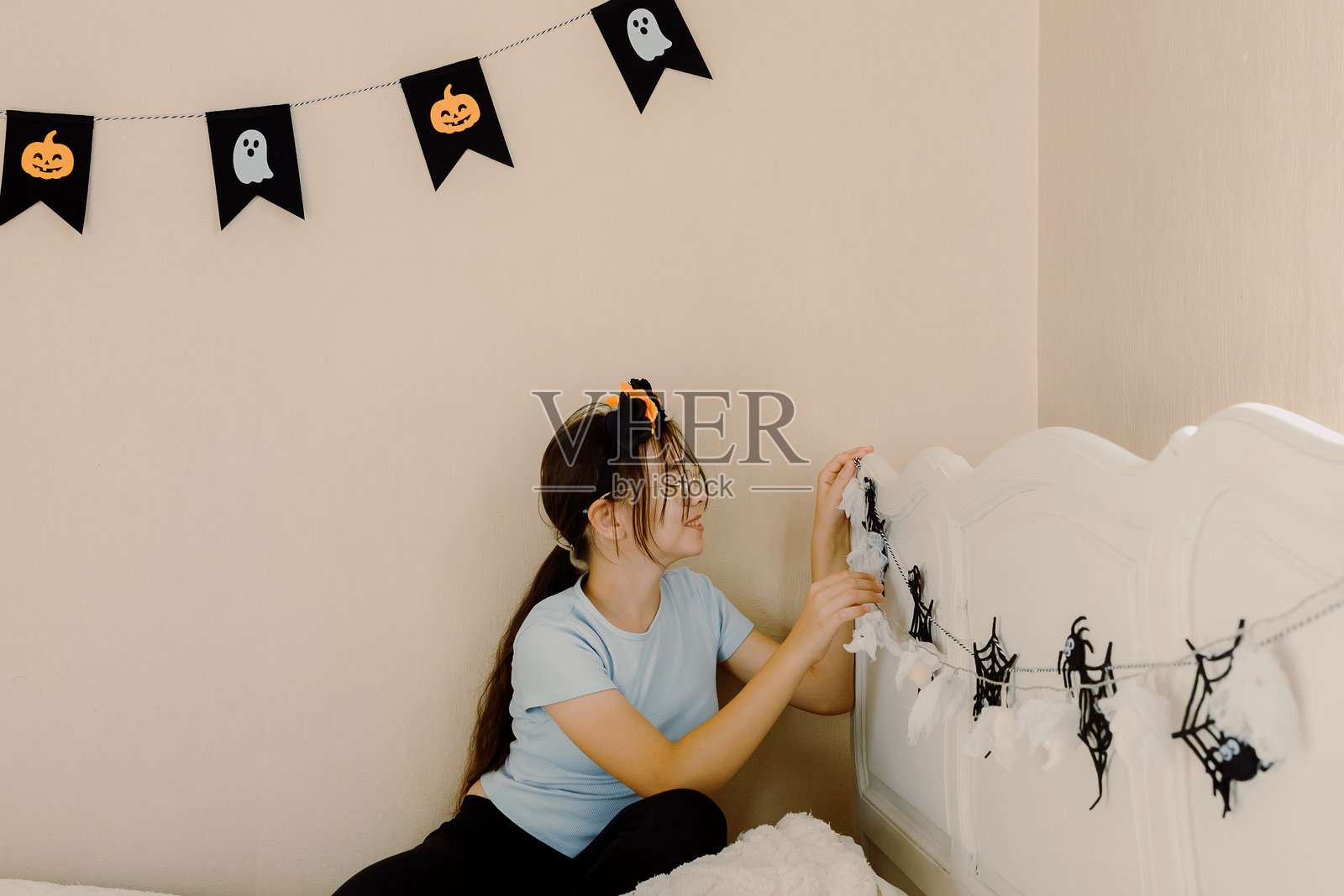 一个女孩在她的床上挂上万圣节鬼魂的花环。照片摄影图片