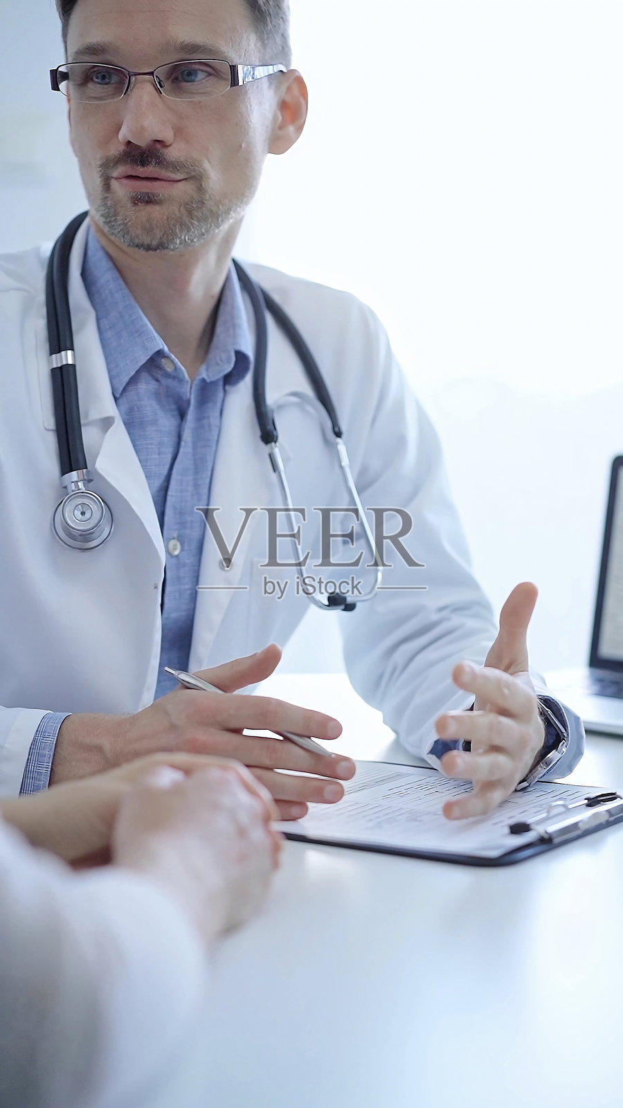 医生与患者。医生穿着白色的医用外套，里面是蓝色衬衫，在诊所咨询时用手势表达。医学概念照片摄影图片