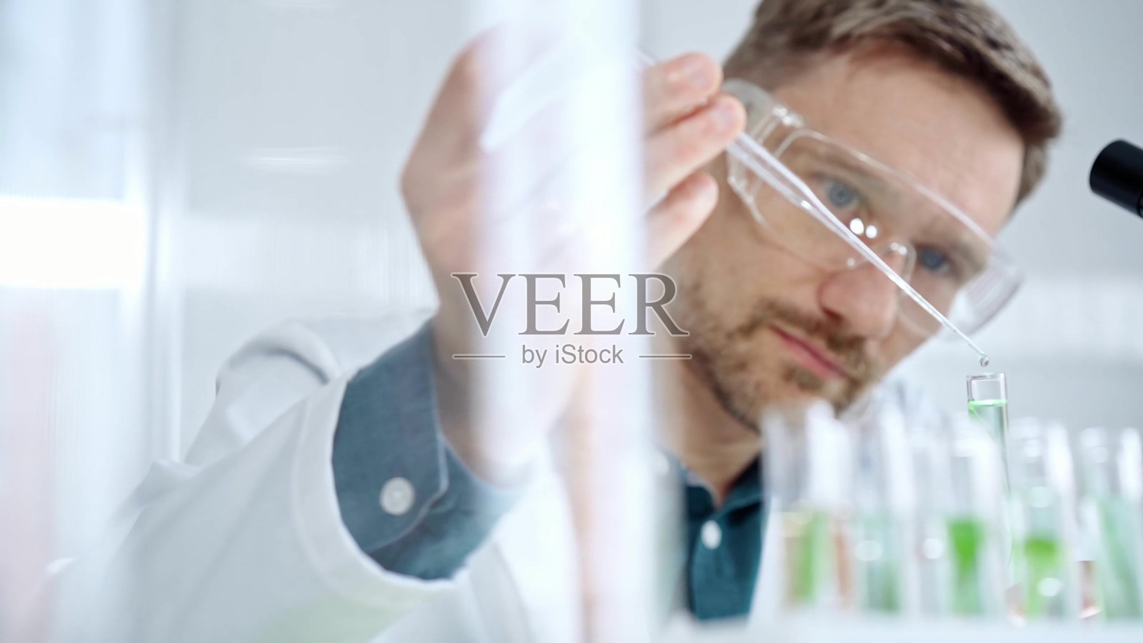 戴着安全眼镜的男子在现代实验室中使用移液管处理实验管，研究人员的特写。科学与医学照片摄影图片