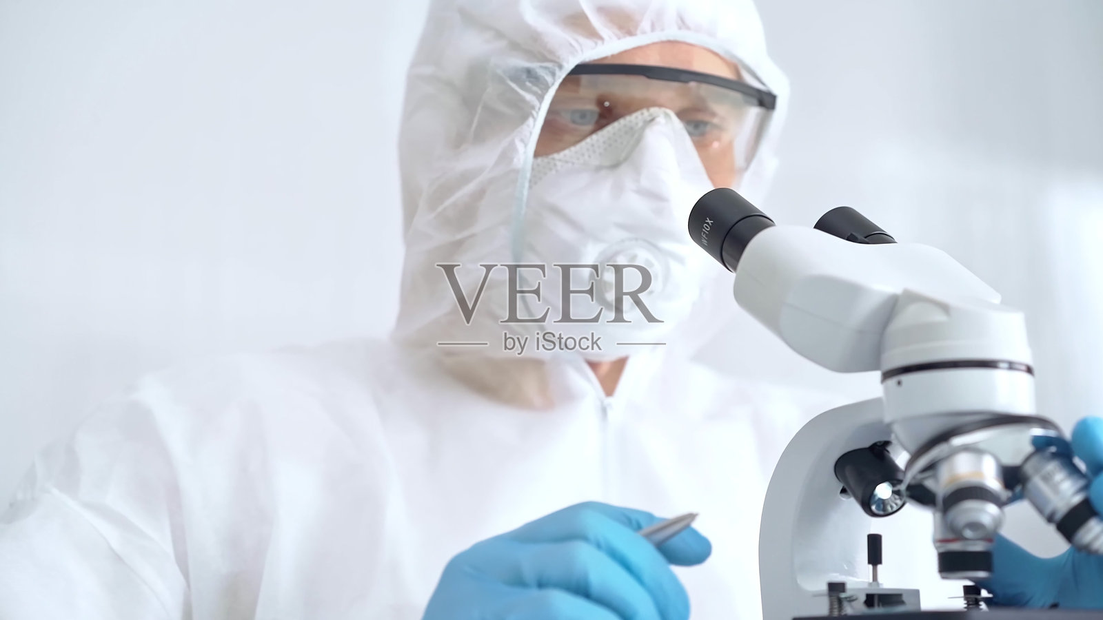科学家在实验室环境中使用显微镜分析样本。专注的研究人员特写，穿着防护装备。科学概念照片摄影图片