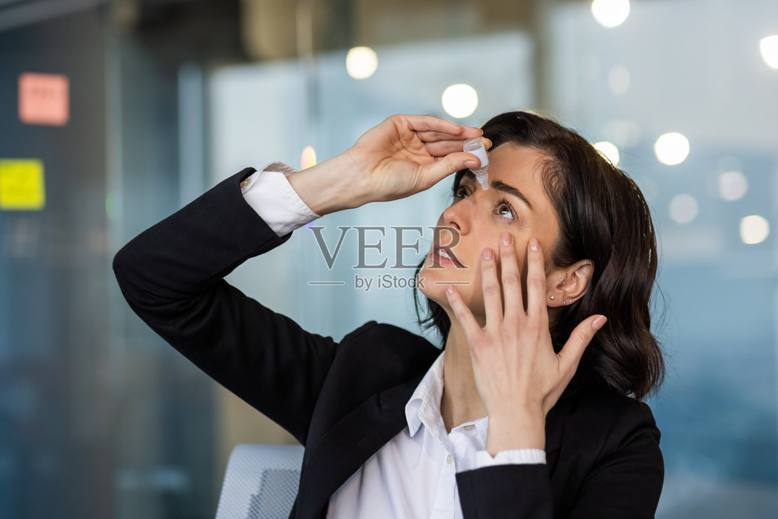 女商人在办公室环境中滴眼药水以缓解干眼症，专注于工作会议中的健康与舒适。照片摄影图片