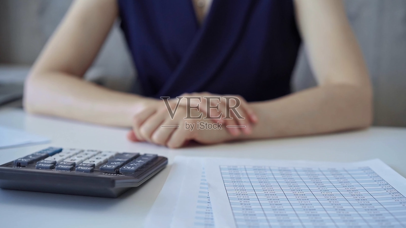 穿着深蓝色裙子的女商人在桌子旁坐着，桌上有财务文件和计算器，正在等待会议开始。照片摄影图片