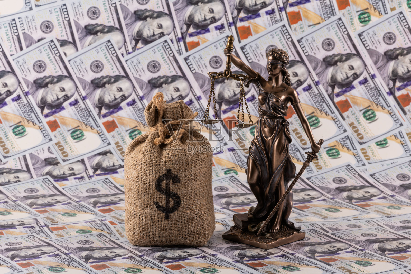 天秤女神雕像与一个带有美元符号的钱袋，置于100美元钞票的背景上照片摄影图片