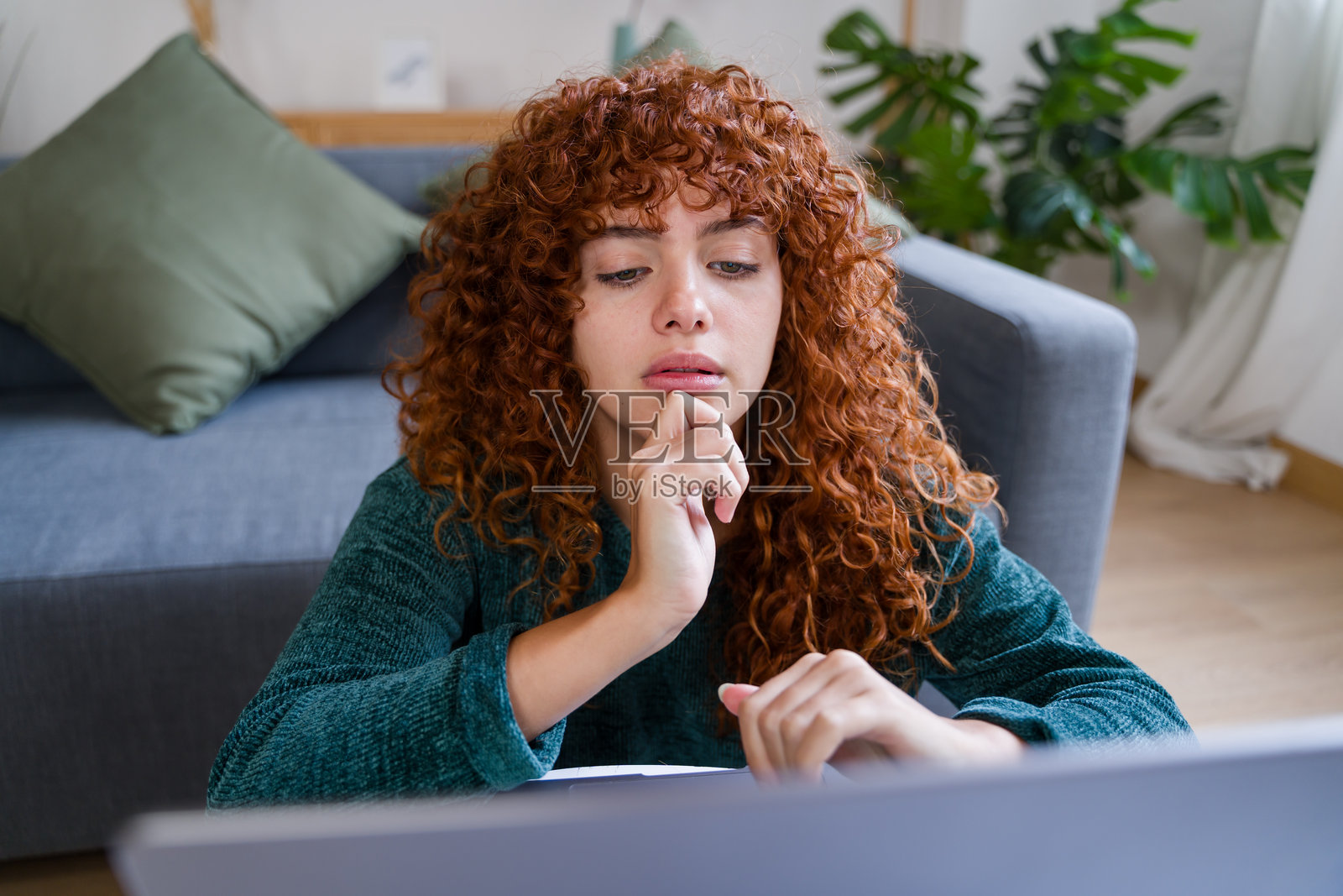 专注的自由职业女性在家中使用笔记本电脑工作，思考时用手托着下巴。照片摄影图片