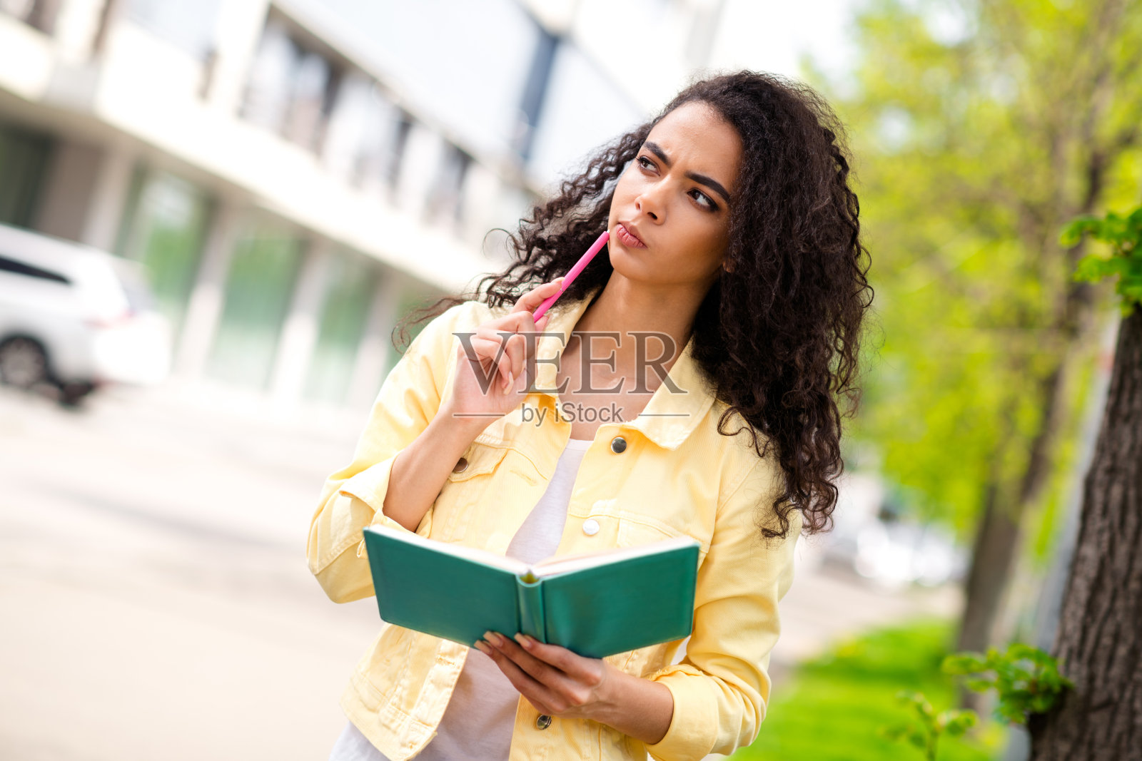 可爱的年轻女孩在户外城市街道上手持笔记本思考。照片摄影图片
