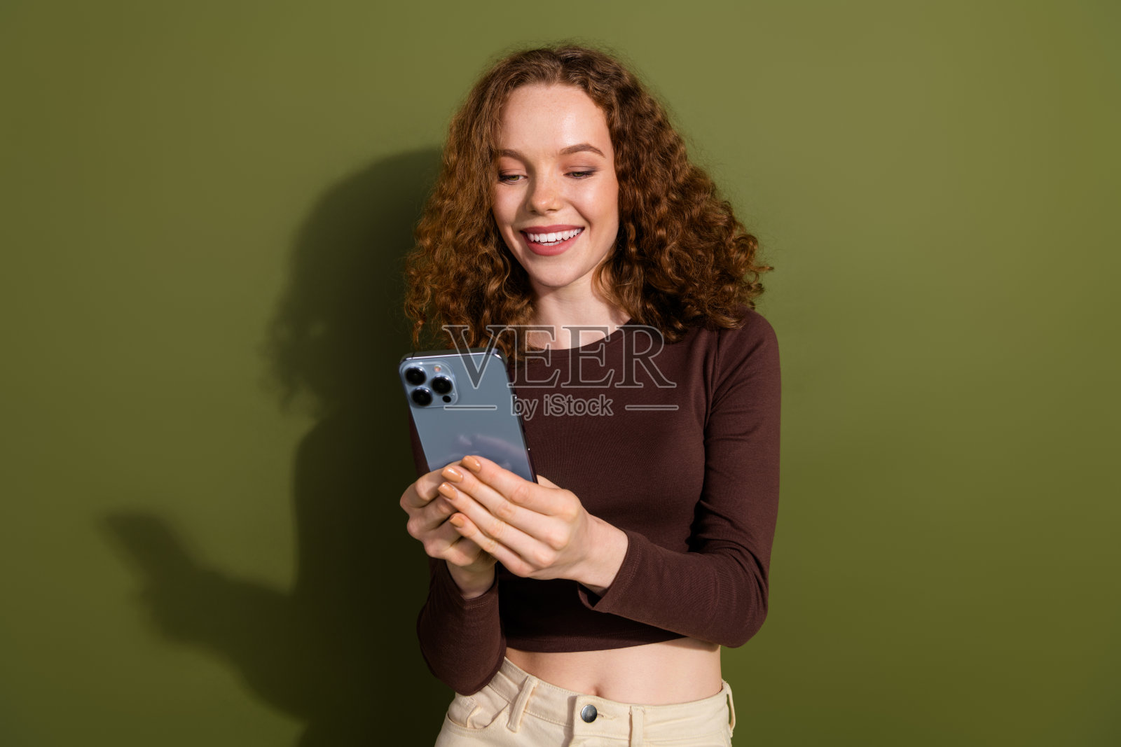 穿着棕色衬衫的迷人积极女孩在绿色背景下聊天，使用Instagram、Twitter、Telegram和Facebook。照片摄影图片