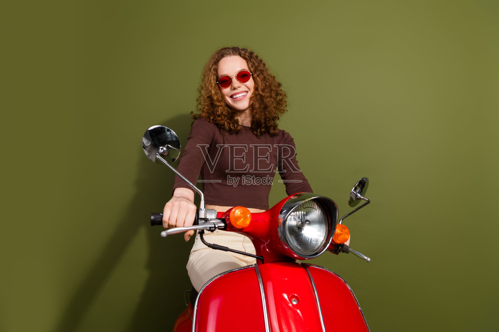 一位穿着棕色服装的光鲜迷人的年轻女士骑着滑板车，背景为空旷的卡其色。照片摄影图片