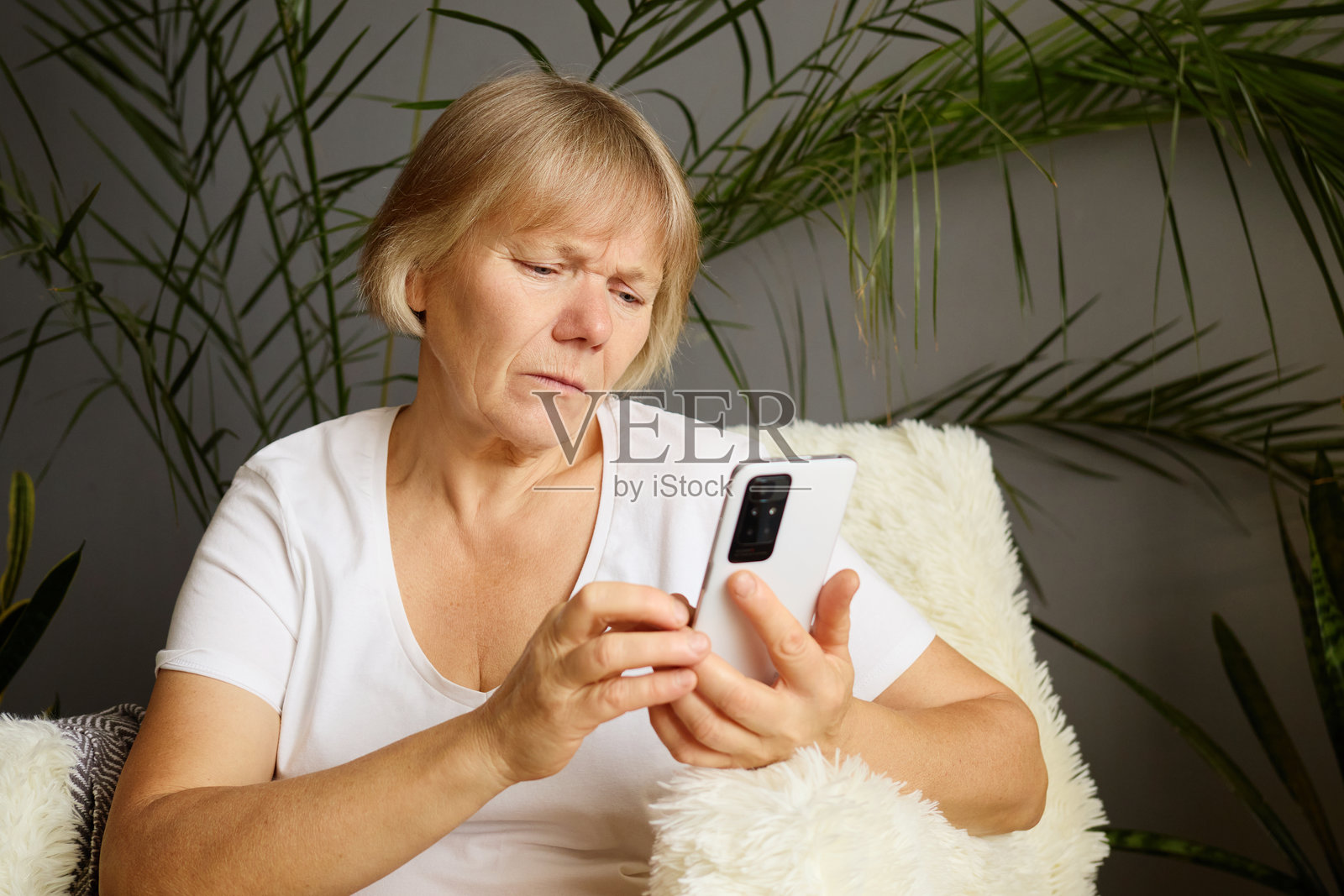 伤心的成熟的女性在家中拿着智能手机，神情沮丧地浏览互联网，查看手机上的在线消息，使用数字技术在社交媒体上聊天。照片摄影图片