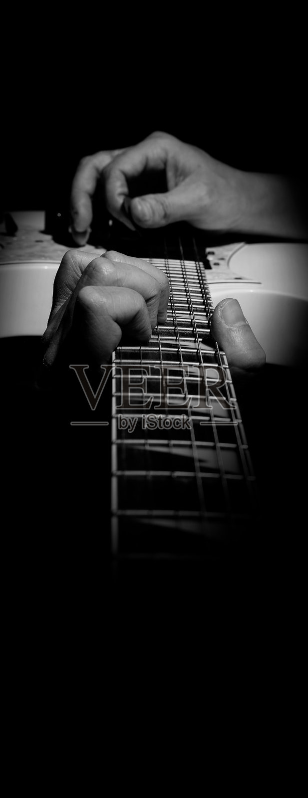 在录音室里弹吉他的吉他手。低调的男人手在白色电吉他上演奏歌曲和翻唱音乐或技能练习。特写镜头展示音乐家在黑色背景下演奏吉他。照片摄影图片