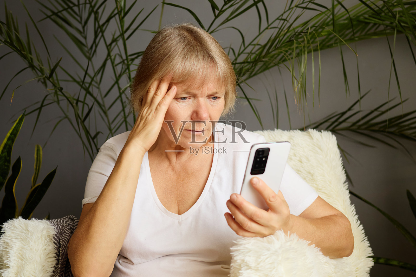 不快乐的老年女性坐在家中，面露不满，使用智能手机浏览在线内容，发信息到社交媒体，感到伤心和沮丧。照片摄影图片