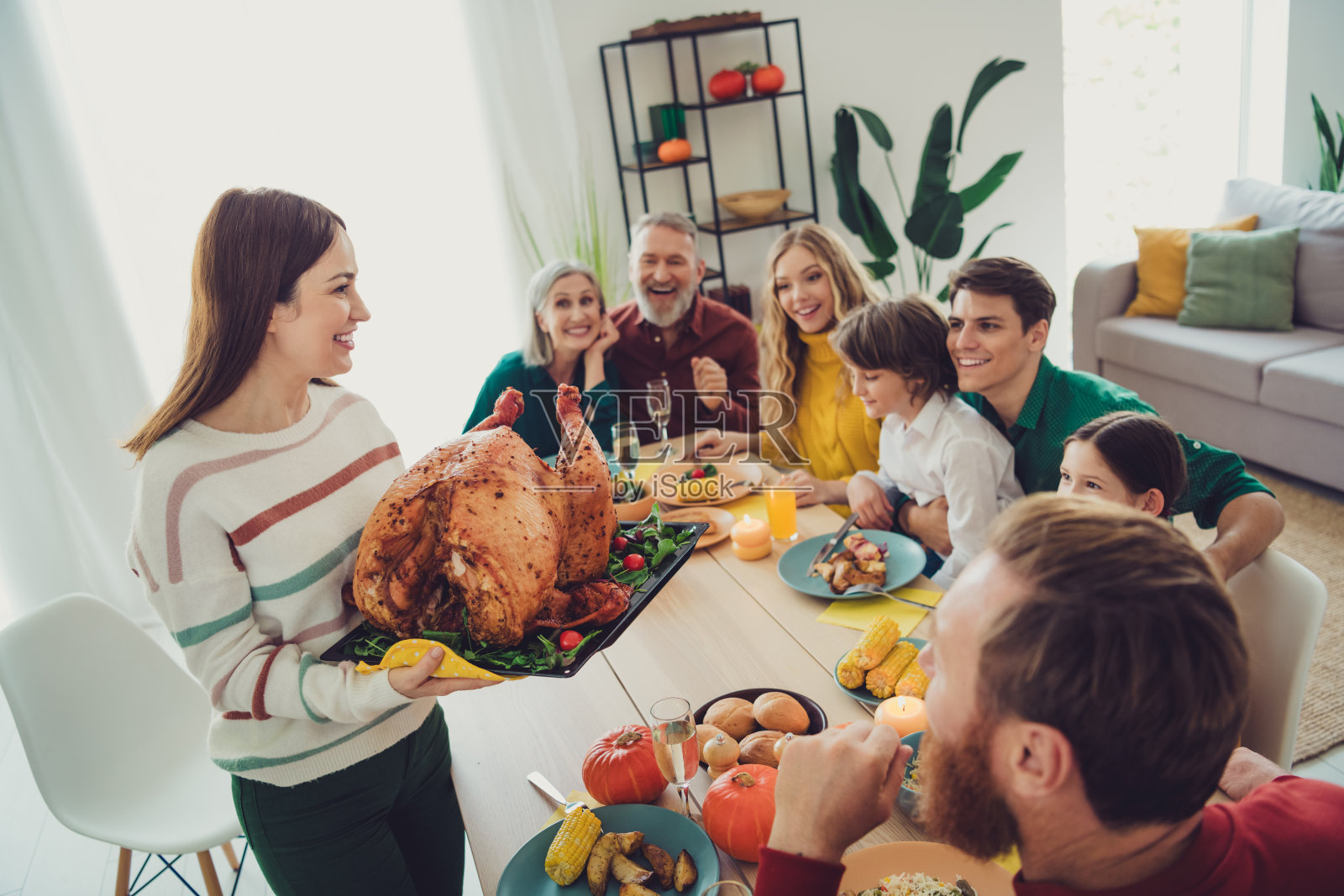 可爱的大家庭在室内一起庆祝感恩节，端上主菜烤火鸡。照片摄影图片