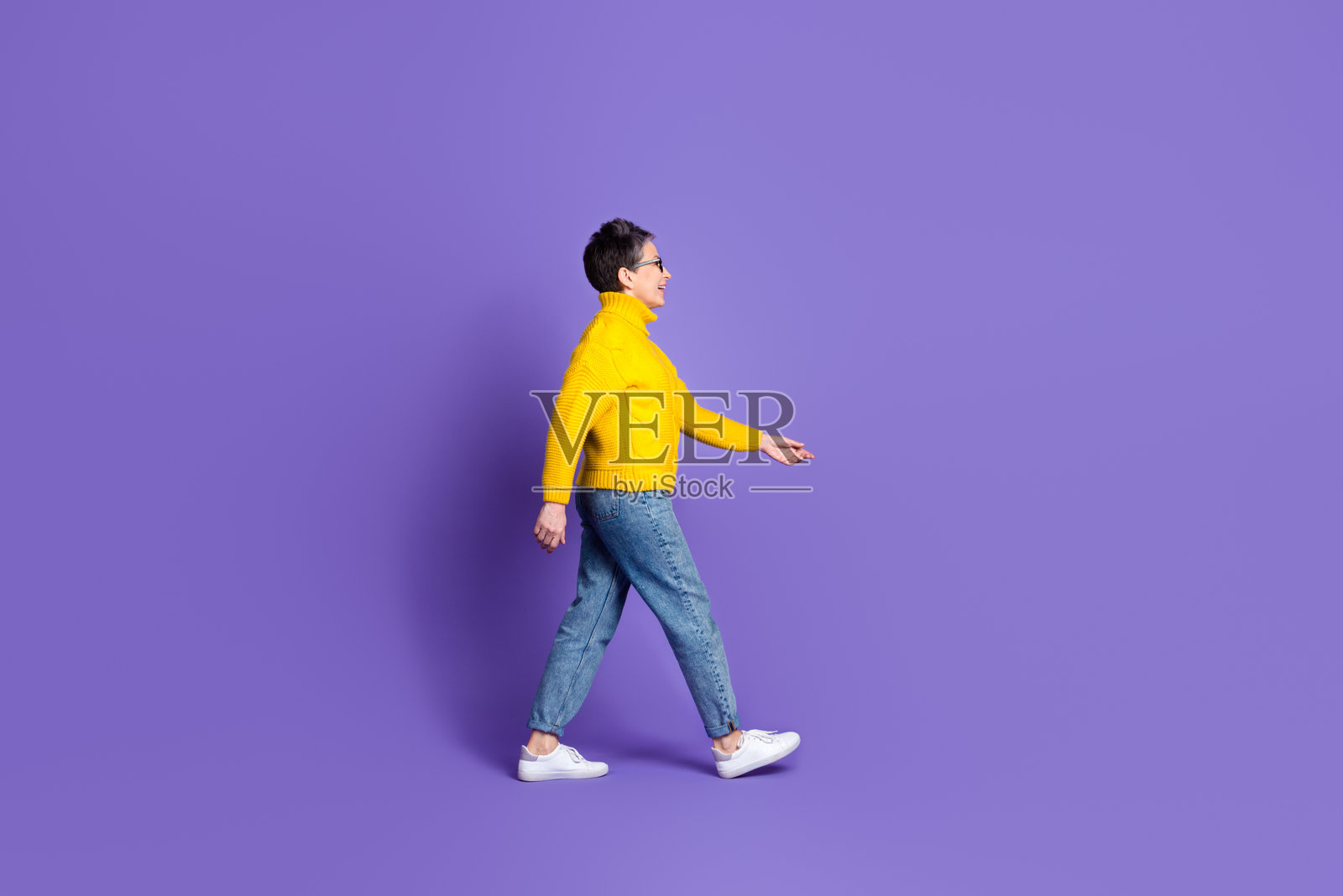 全身照，迷人积极的女性穿着黄色毛衣，在空旷的空间中走动，背景为紫色。照片摄影图片