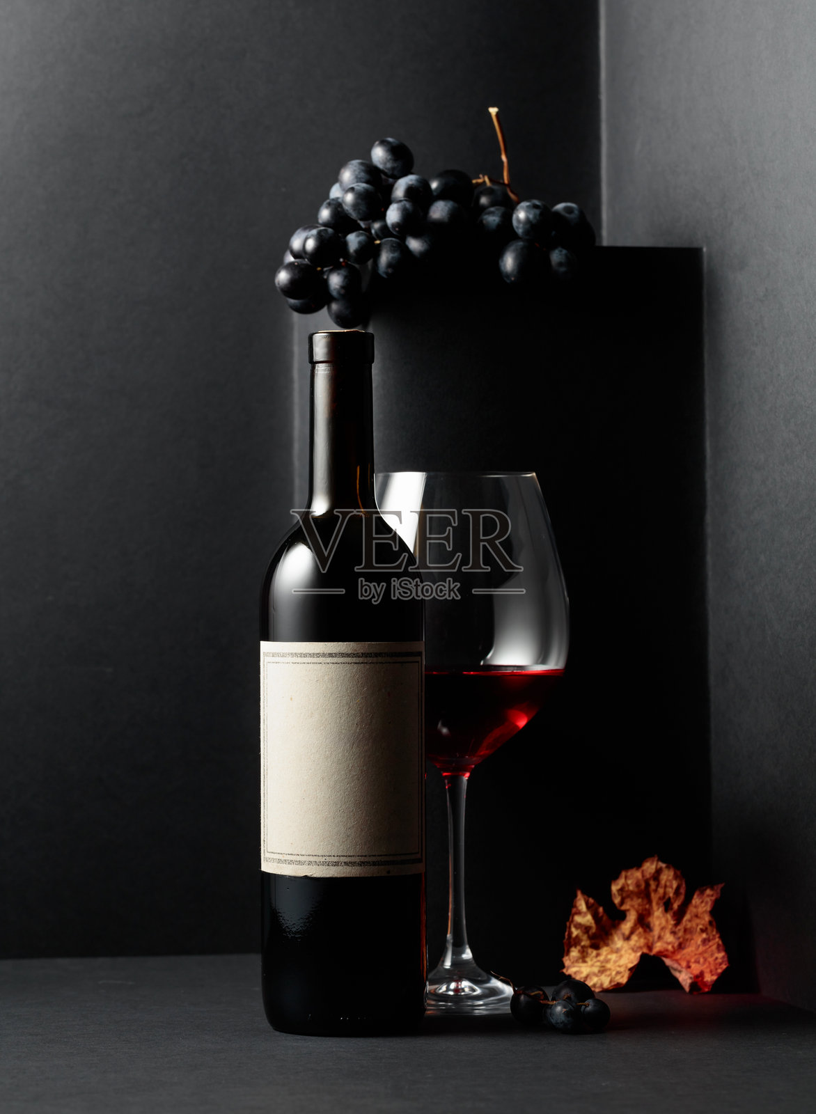 红酒和蓝色葡萄，干枯的藤叶在黑色背景上。照片摄影图片