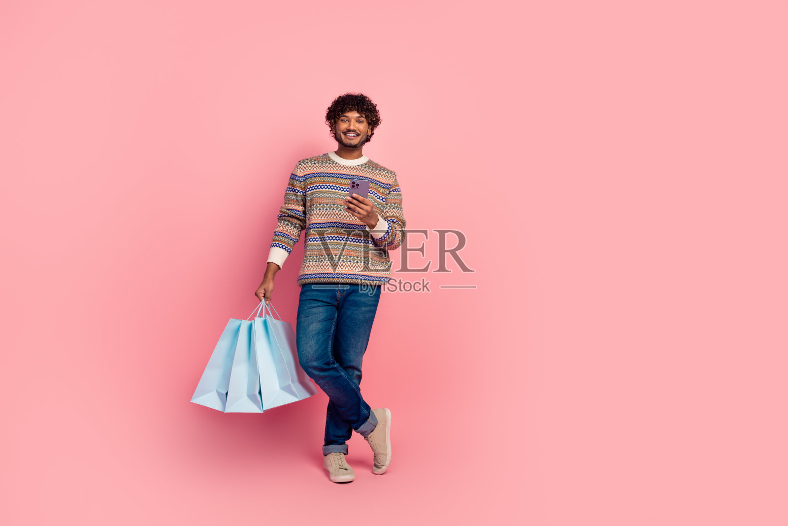 全身肖像，年轻帅气的男士穿着毛衣，手持手机和包，背景为粉色。照片摄影图片