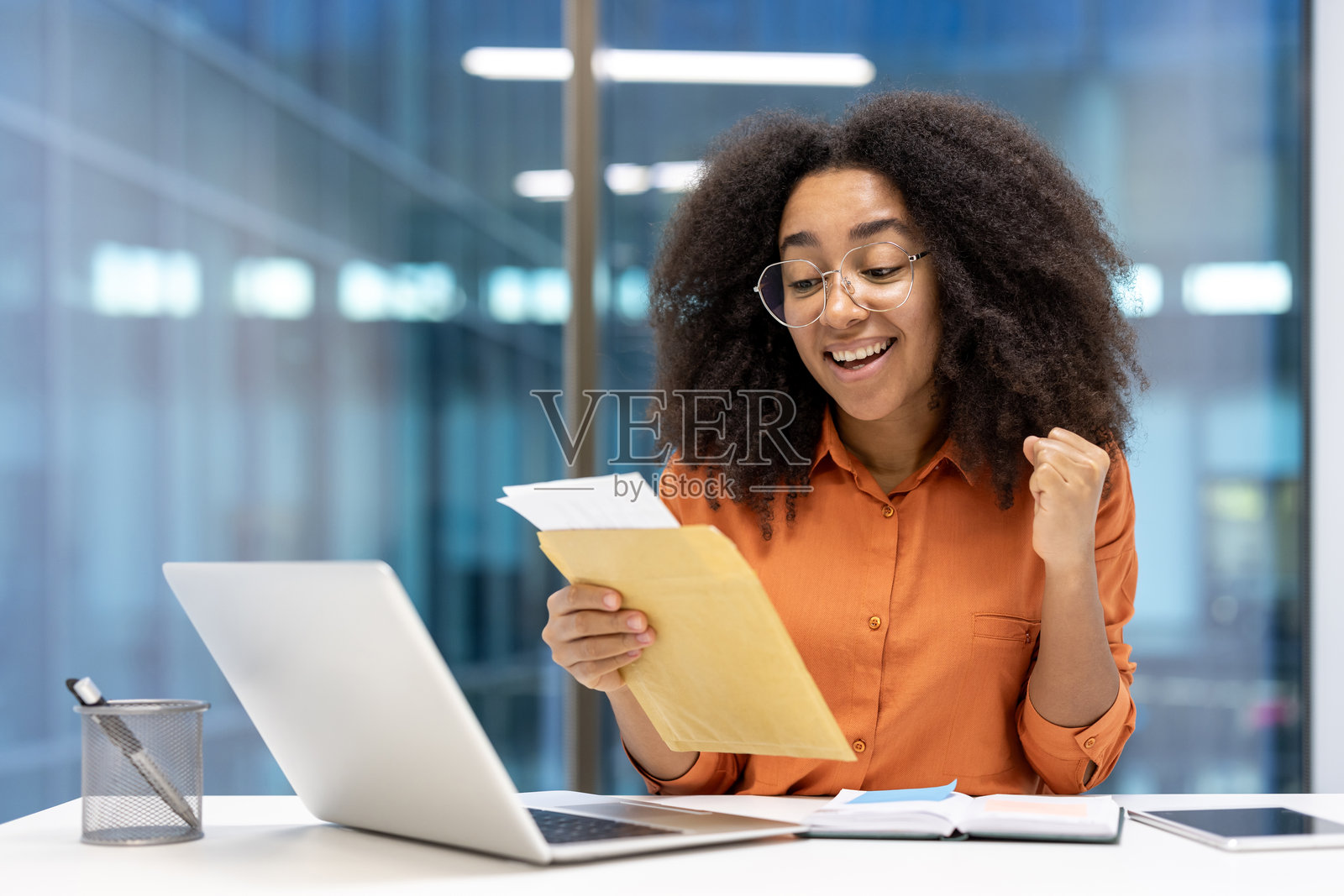 快乐的女性在工作中通过信件收到好消息，庆祝在现代办公室环境中的成功，体现了幸福、成功、成就和沟通重要性的概念。照片摄影图片