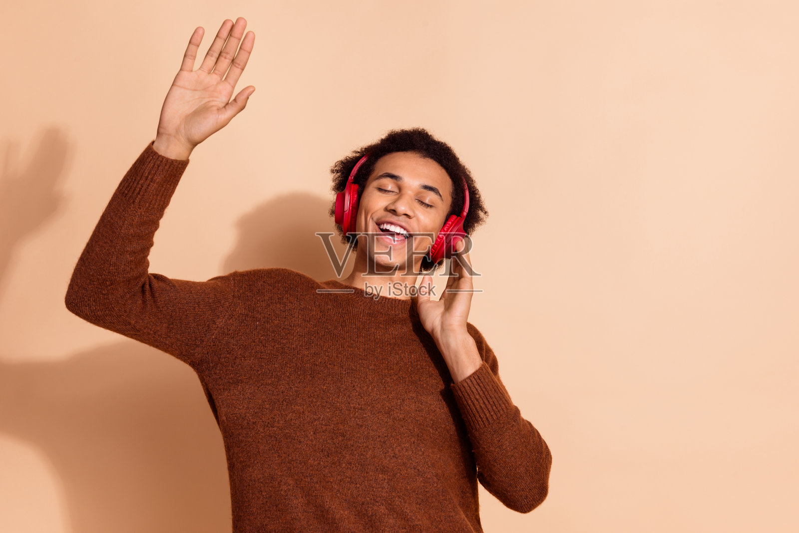 年轻男子在米色背景下戴着红色耳机享受音乐，感到快乐和放松照片摄影图片