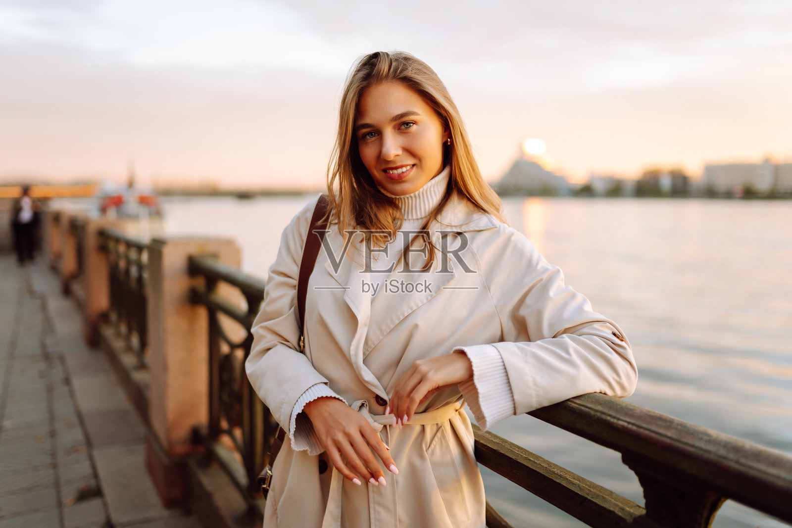 一位年轻女性沿着堤岸漫步，享受温暖的秋日落日。照片摄影图片