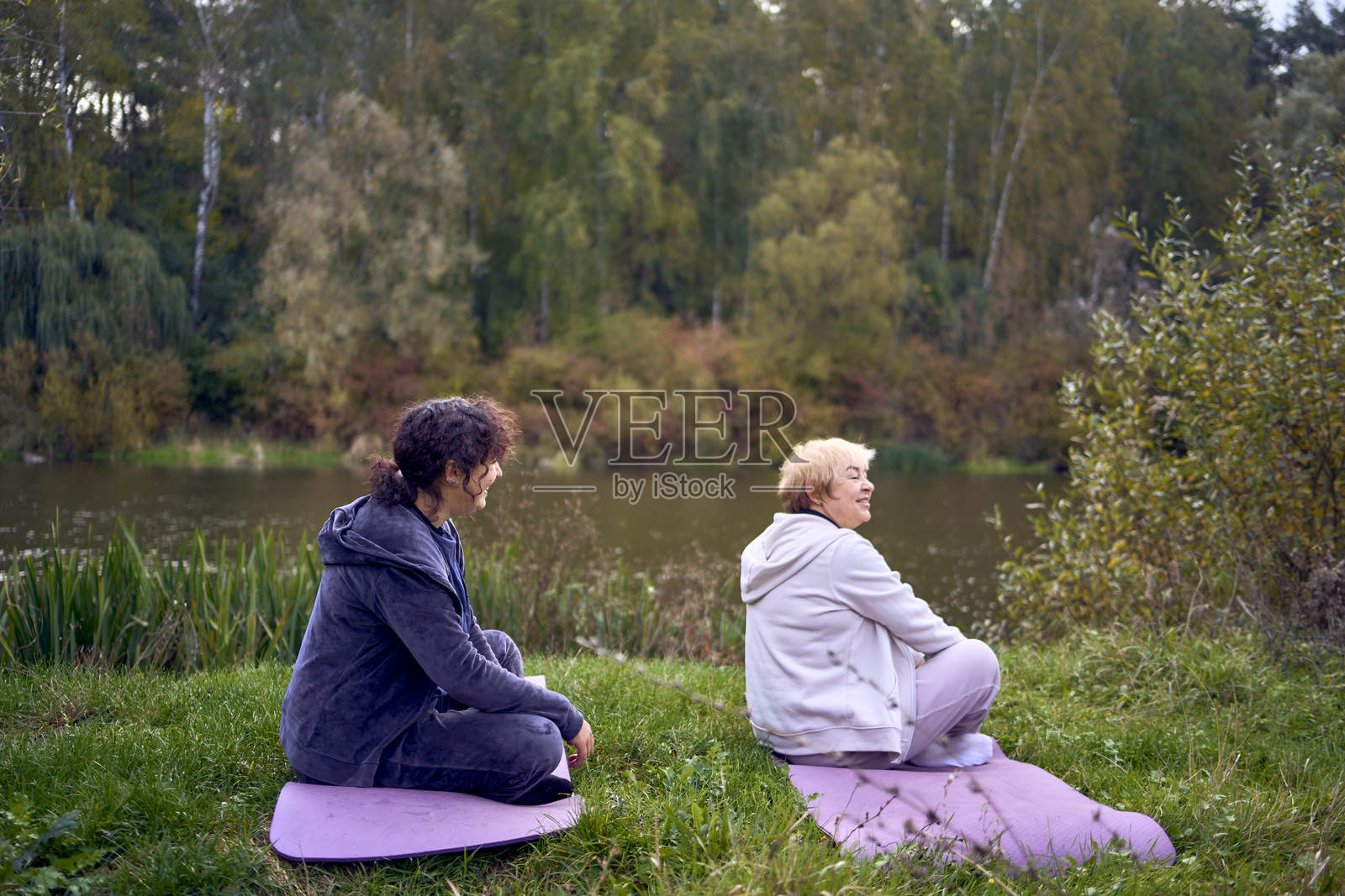 中年女性在秋天的河边教她的老母亲进行身体锻炼和瑜伽以保持健康照片摄影图片