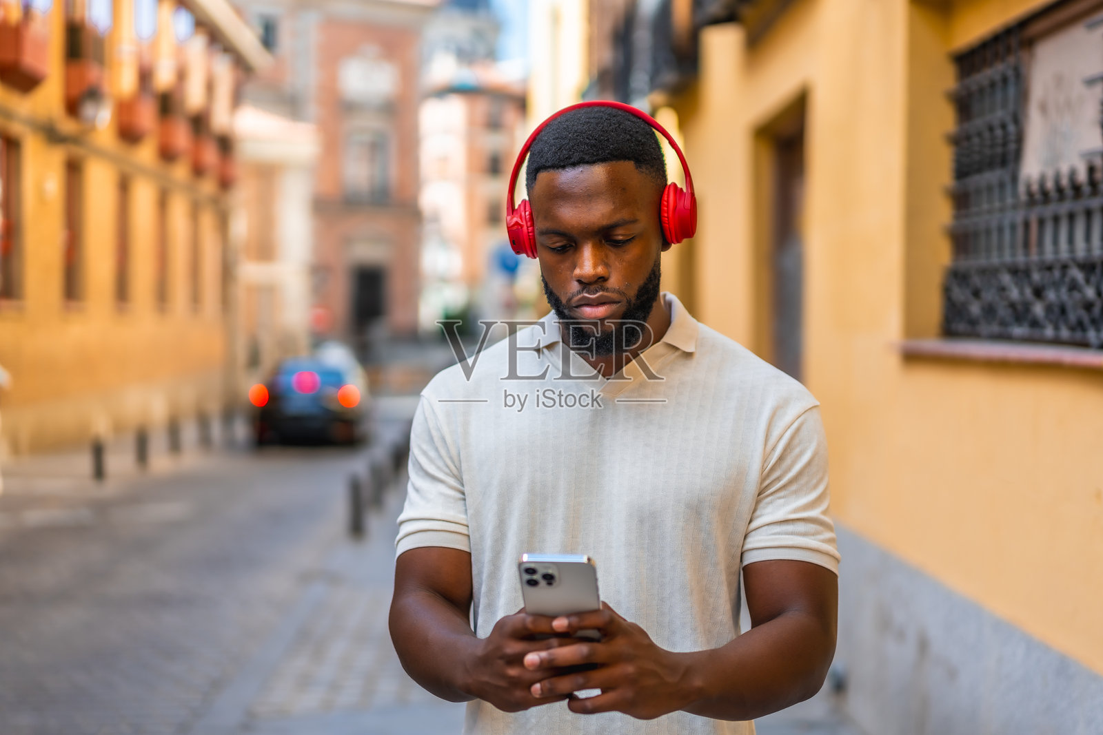 非洲男子在街上走路，使用手机和耳机照片摄影图片
