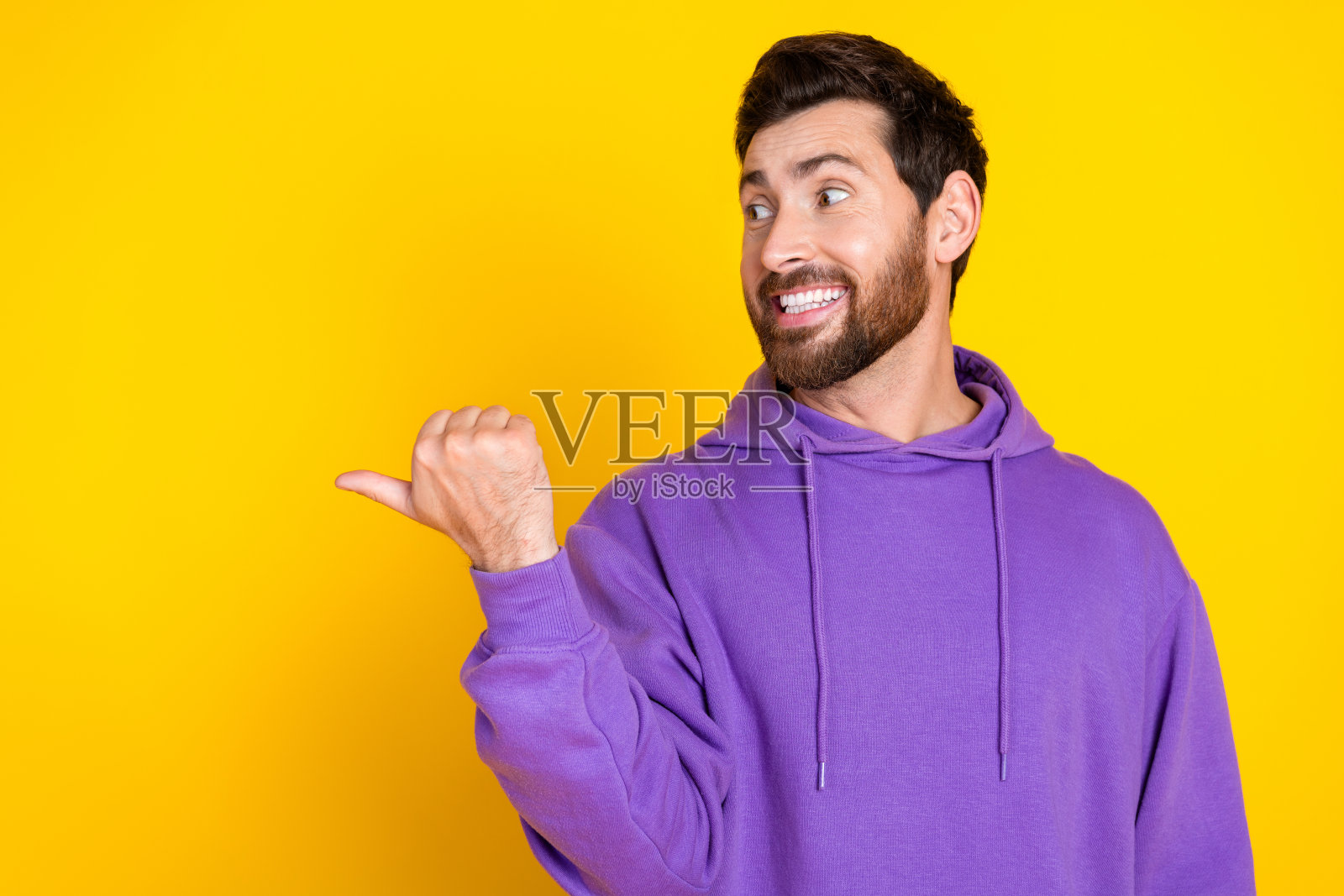 穿着紫色连帽衫的搞笑男子，时尚的短须，目光注视着黄色背景上空荡荡的折扣空间。照片摄影图片