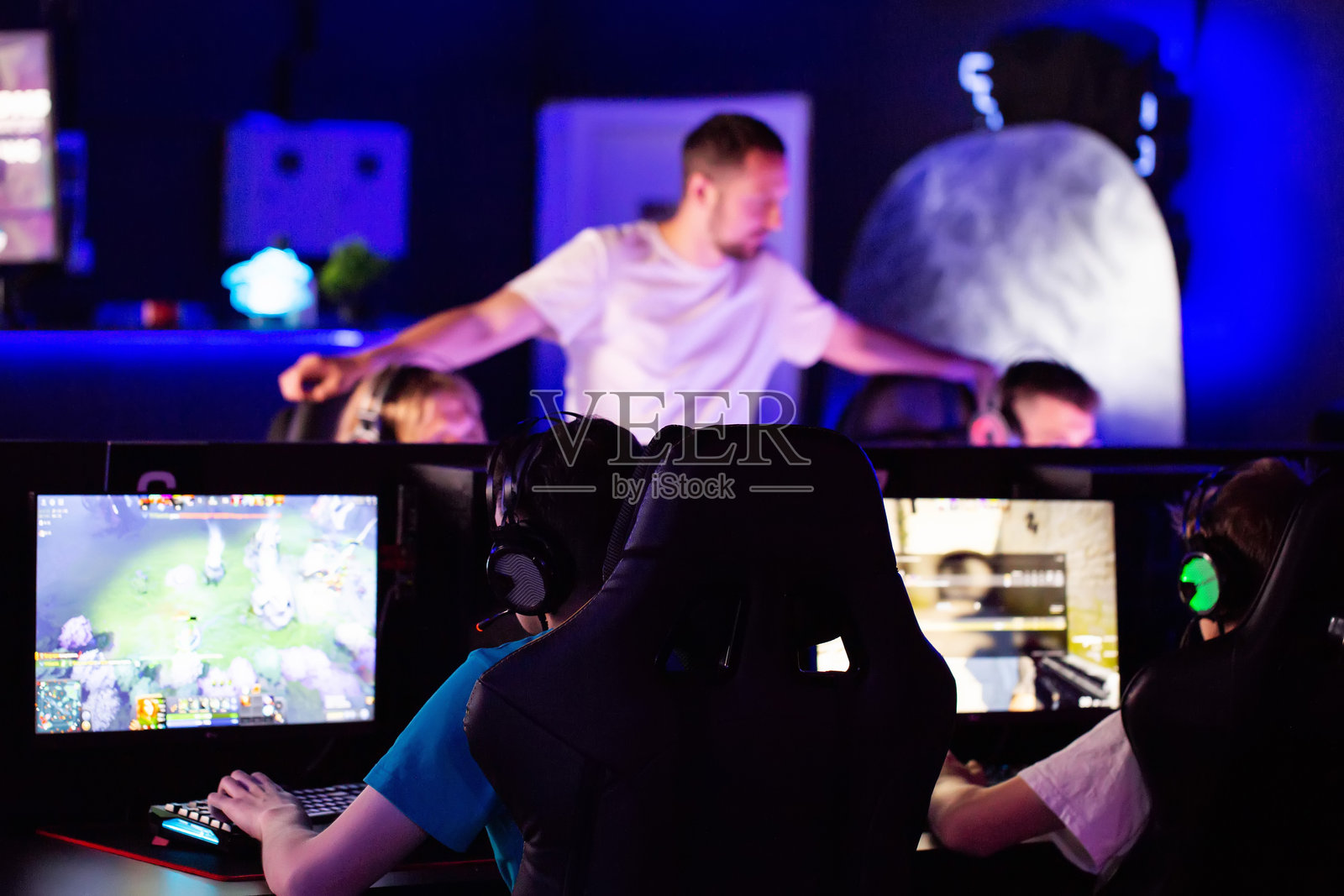 电子竞技教练正在观看训练者的评论，并向他的队员们提供指导。戴着耳机的玩家在电脑俱乐部的比赛中玩视频游戏，属于电子竞技团队。战术、策略、情感特写。照片摄影图片