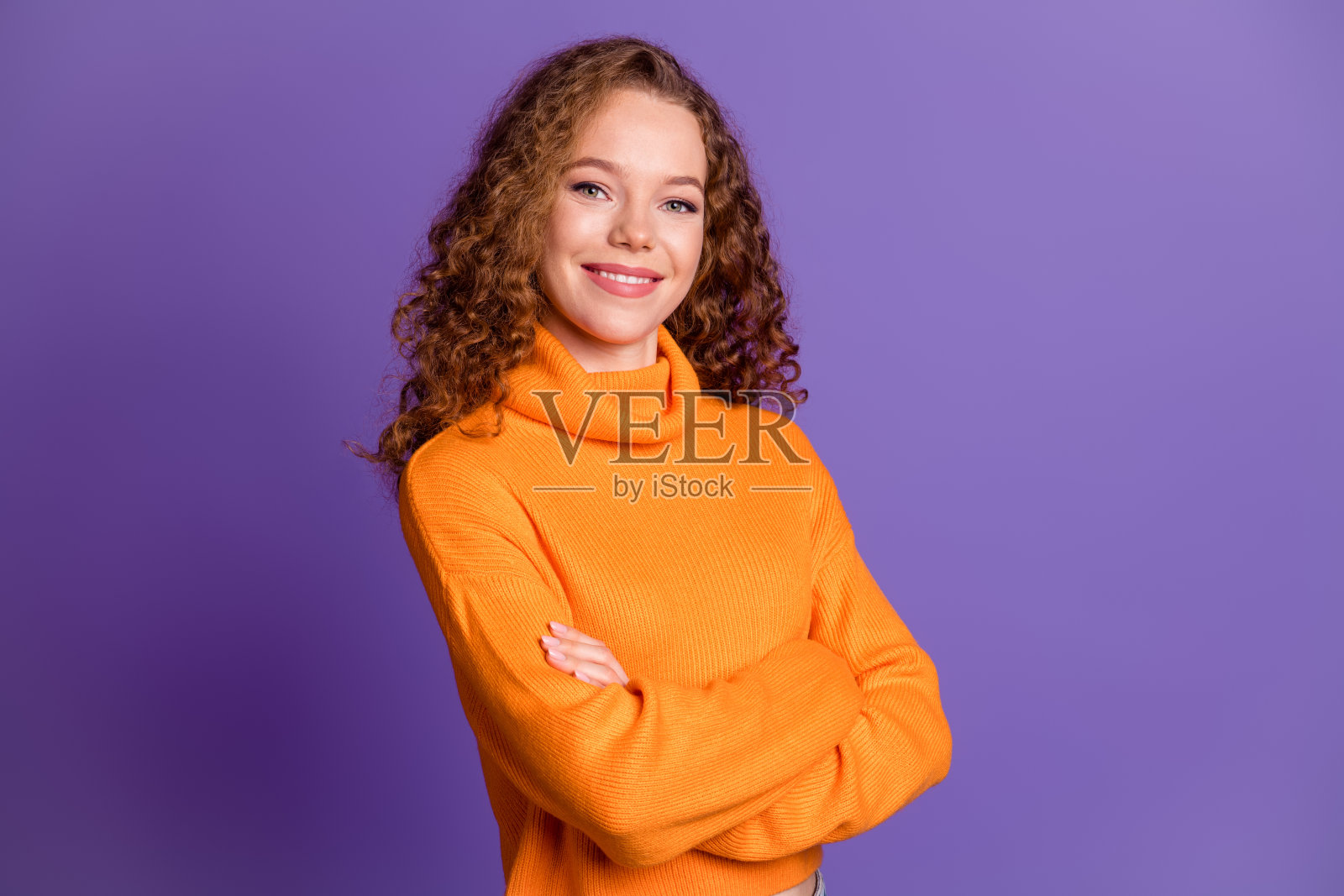 自信可爱的女孩穿着时尚的橙色衣服，双臂交叉，背景为紫色。照片摄影图片